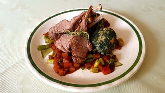 Ein Teller mit Lammrippchen, buntem Gemüse und Spinatknödel.