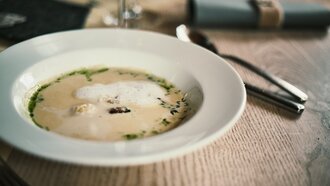 Eine elegante Suppe mit Schaum und Kräutern auf einem weißen Teller.
