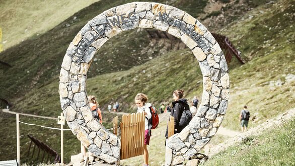Kinder und Erwachsene passieren ein großes steinernes Tor auf einem Wanderweg.