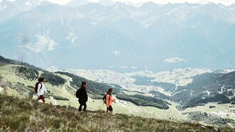 Drei Wanderer erkunden die Alpenlandschaft mit Bergen im Hintergrund.
