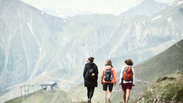 Drei Frauen wandern auf einem Bergweg in der Natur.