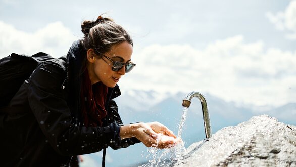 Frau wäscht sich die Hände unter einem Wasserhahn im Freien.