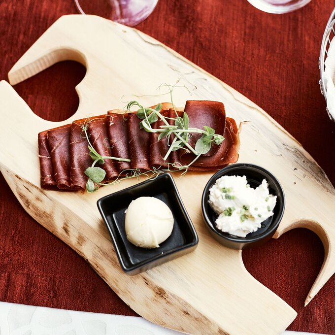 Gourmetplatte mit geschnittenem Fleisch, Dips und Kräutern auf einem Holzbrett.