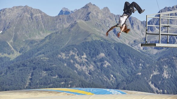 Ein Athlet springt spektakulär von einer Plattform in die Berge.