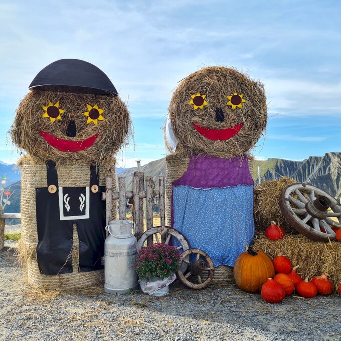 Two hay figures in outfits surrounded by pumpkins.