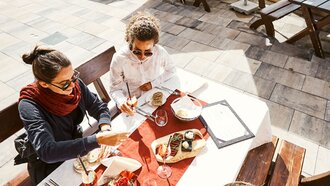 Drei Personen genießen ein Mittagessen auf einer Terrasse in den Bergen.