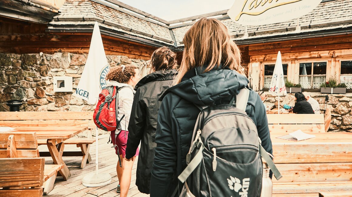 Drei Wanderer gehen zu einem rustikalen Bergrestaurant.