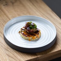 Ein kunstvoll angerichtetes Gericht mit Fleisch, Zwiebeln und Saucen.