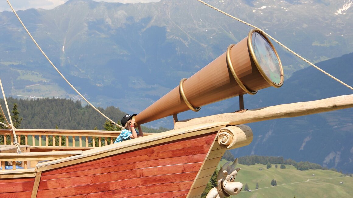 A boy gazes through a large telescope on a wooden ship.
