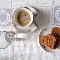 Eine Tasse Kaffee und Herzwaffeln auf einer dekorativen Tischdecke.