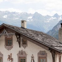 Detailansicht eines Hauses mit kunstvollen Wandmalereien und Bergen im Hintergrund.