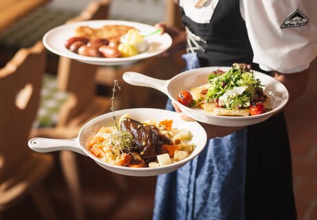 A waitress carries three plates of traditional German dishes.