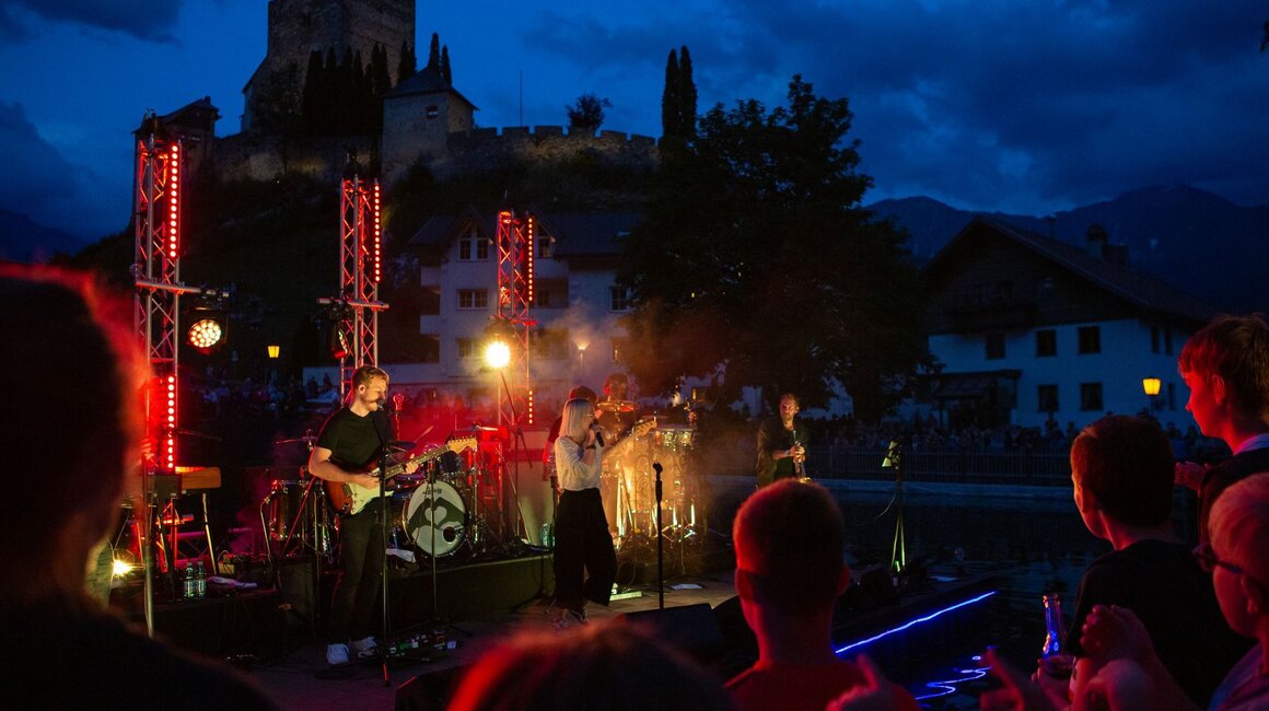 Band spielt bei einem Konzert im Freien mit beleuchtetem Hintergrund.