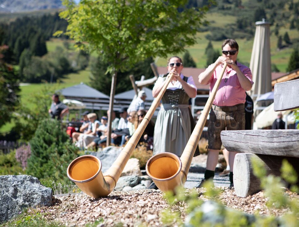 Zwei Musiker spielen Alphorn in einer malerischen Alpenlandschaft.