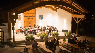 Eine Musikkapelle spielt auf einer Bühne im Freien bei Nacht.