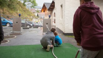 Zwei Kinder sitzen und spielen mit einem Wasserschlauch im Freien.