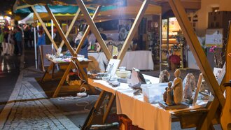 Abendliche Marktstandaufnahme mit Handwerkskunst und Statuen.