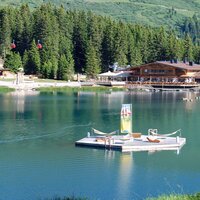 Ein ruhiger See umgeben von Bäumen mit einer Berghütte im Hintergrund.