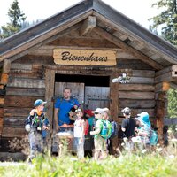 Eine Gruppe Kinder vor einem Holzhaus in der Natur.