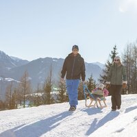 Ein Paar mit einem Kind auf einem Schlitten im Schnee.
