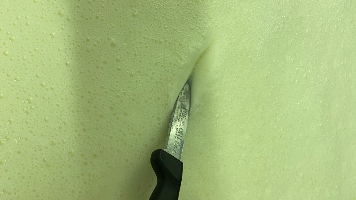 Eine Hand hält ein Messer, das durch Schaum schneidet.