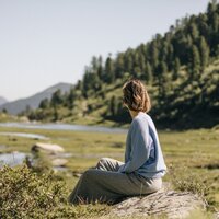 Eine Frau sitzt am Ufer eines ruhigen Flusses in der Natur.