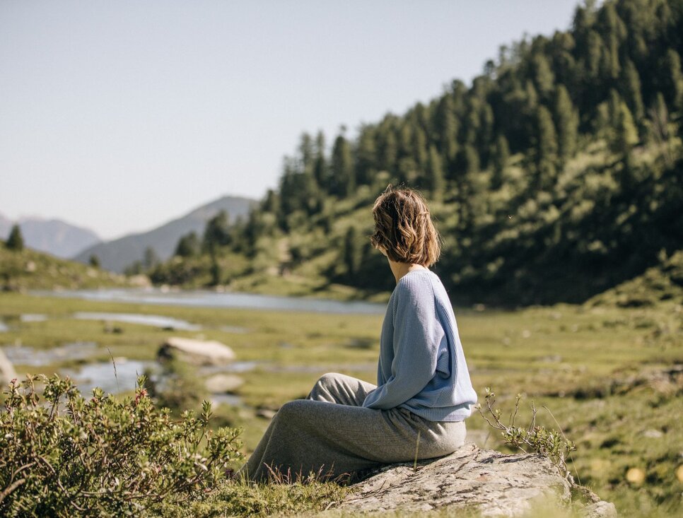 Eine Frau sitzt am Ufer eines ruhigen Flusses in der Natur.