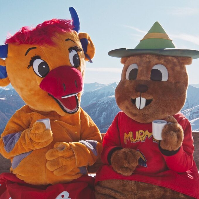 Zwei Maskottchen, ein Rind und ein Biber, genießen die Aussicht in den Bergen.