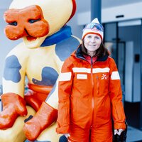 Eine Frau in einer roten Skijacke und Mütze steht neben einer bunten Skulptur.